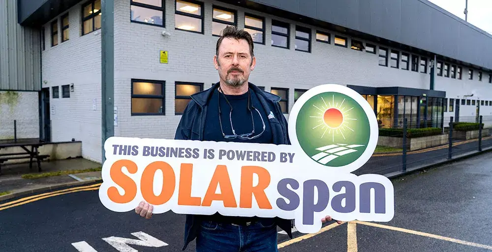 Adrian Madden, Facilities Manager at Primus POD, holding a “This business is powered by SOLARspan” sign at a High Spec Manufacturing facility following a commercial solar PV Solar Project in Ireland using Van Der Valk Solar Systems